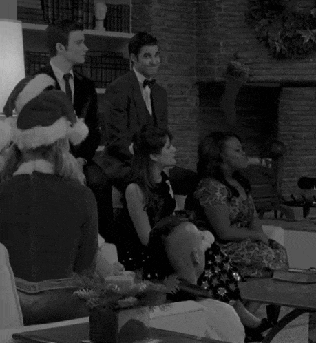a black and white photo of a group of people sitting around a fireplace