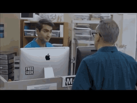 a man is talking to another man in front of an apple computer with a free geek sticker on it