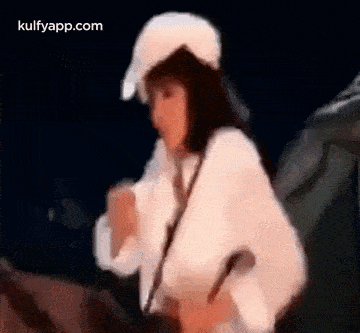 a woman wearing a white hat and a white sweater is standing in front of a microphone .