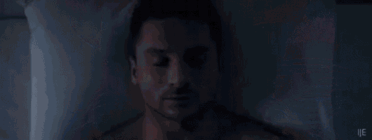 a shirtless man is laying in bed with his eyes closed and his head on a pillow .