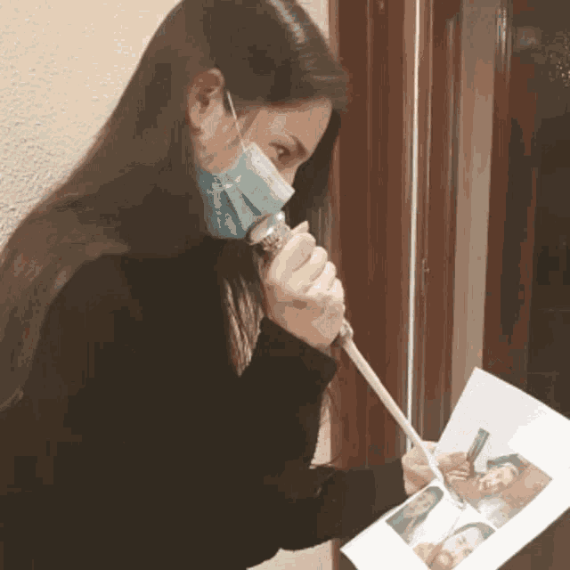 a woman wearing a face mask is holding a stick and looking at a picture