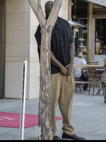 a man standing next to a tree in front of a store that says wine shop