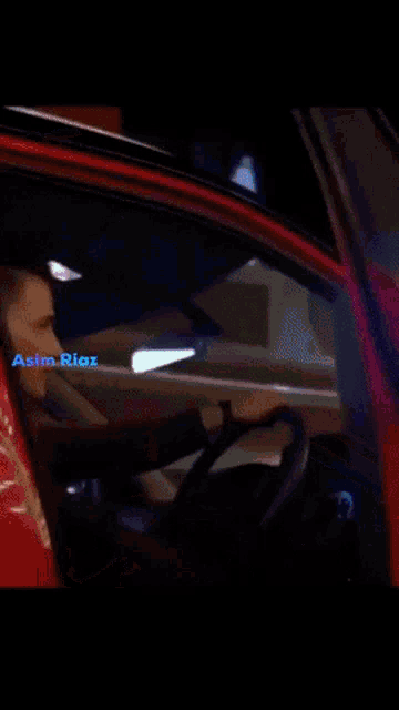 a man in a red suit is sitting in a dark room with asim riox written on the bottom