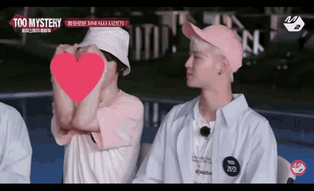 two men wearing pink hats are making a heart shape with their hands
