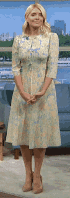 a woman in a floral dress is standing in front of a couch .