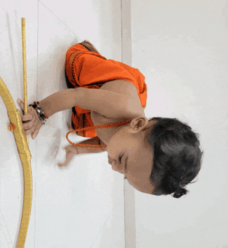 a little boy in an orange outfit is holding a gold bow and arrow