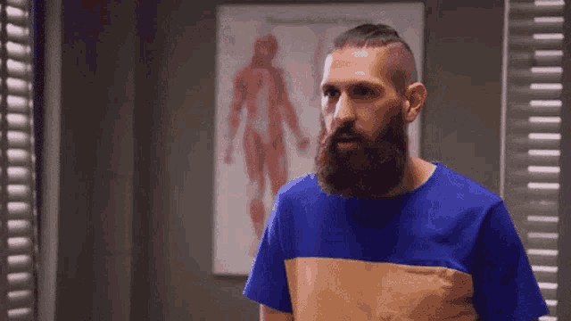 a man with a beard is standing in front of a picture of a man 's muscles .
