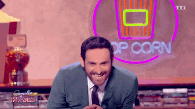 a man in a suit and tie is smiling in front of a sign that says popcorn