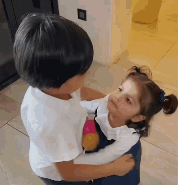 a boy is holding a little girl in his arms and the little girl is looking at the boy .