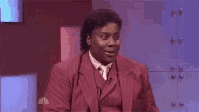 a man in a red suit and tie is making a surprised face while sitting on a stage .