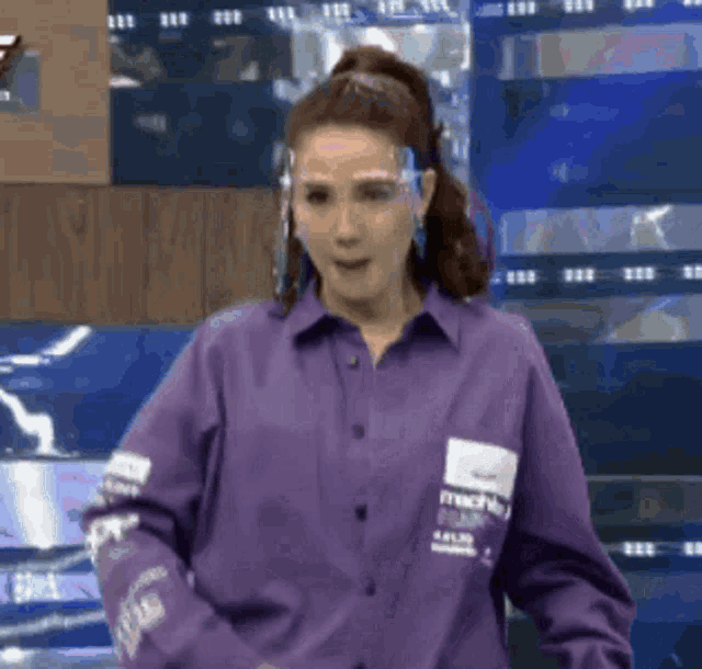 a woman in a purple shirt and face shield is dancing on a stage .