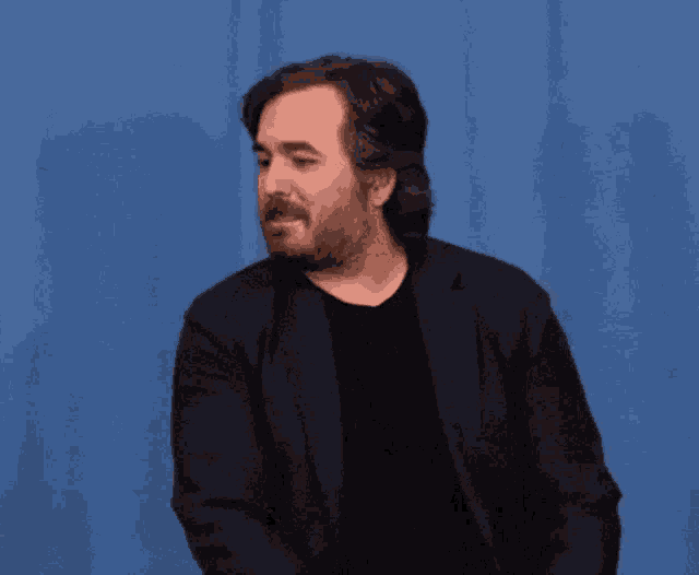 a man with a beard wearing a black shirt and a black jacket