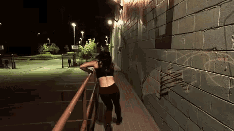 a woman leans against a railing in front of a brick wall with graffiti on it that says ' n '