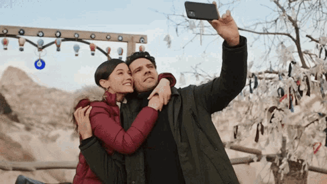 a man is taking a selfie with his phone while a woman hugs him