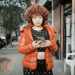 a woman wearing an orange jacket looks at her phone