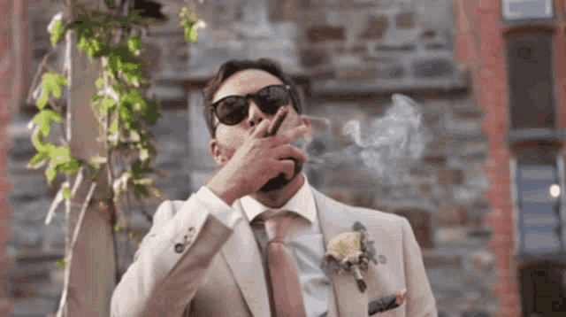 a man in a suit is smoking a cigarette in front of a stone building .