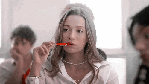 a young woman is holding a red pen in her mouth while sitting in a classroom .