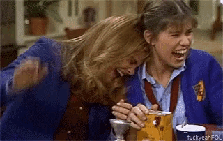 two women are laughing together while sitting at a table with a cup of coffee .