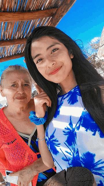 two women posing for a picture with one wearing a blue and white dress with palm trees