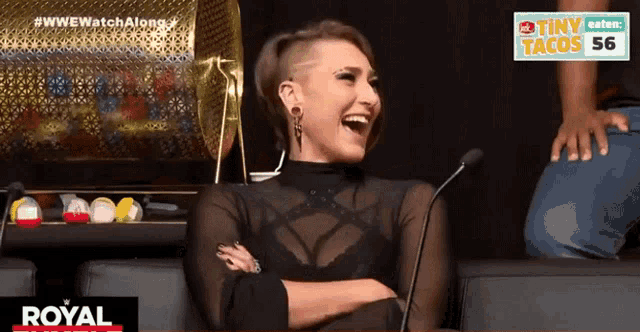 a woman laughs while sitting in front of a microphone in front of a sign that says royal
