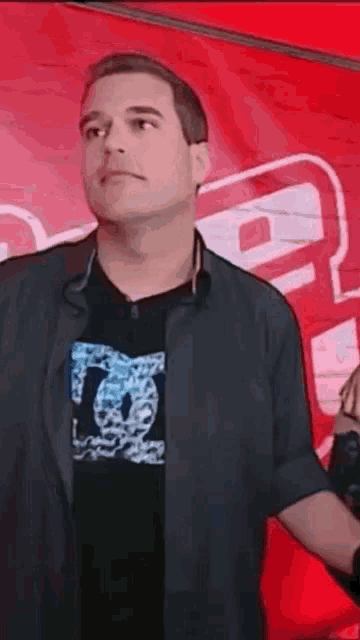 a man wearing a dc shirt stands in front of a red banner