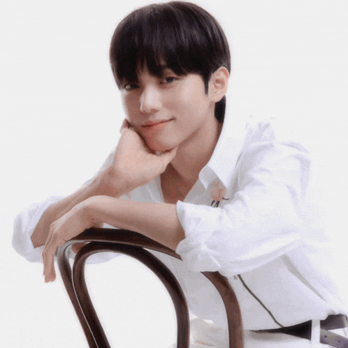 a young man in a white shirt is leaning on a chair