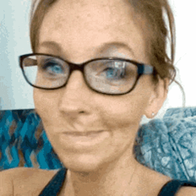 a woman wearing glasses and a black tank top is smiling for the camera .