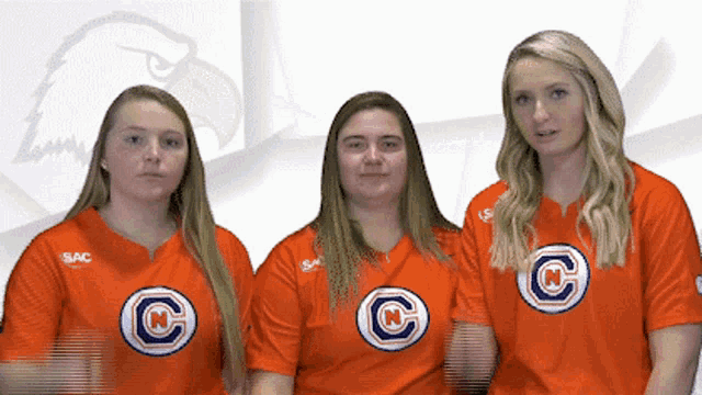 three girls wearing orange shirts with letters c and n on them