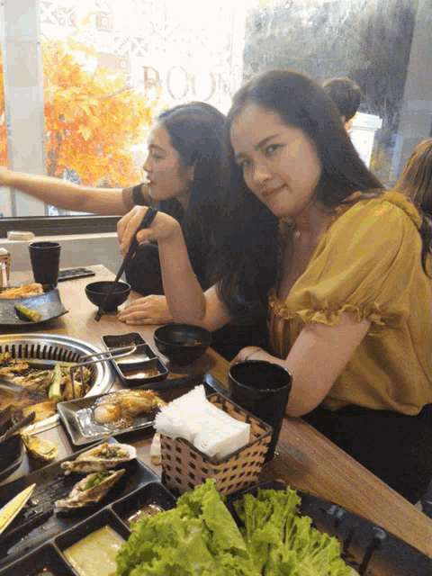 two women sit at a table with plates of food and a basket of lettuce