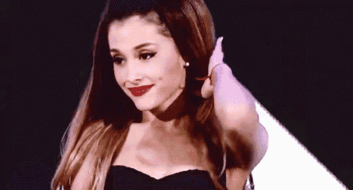 ariana grande is wearing a black strapless dress and red lipstick and holding her hair .