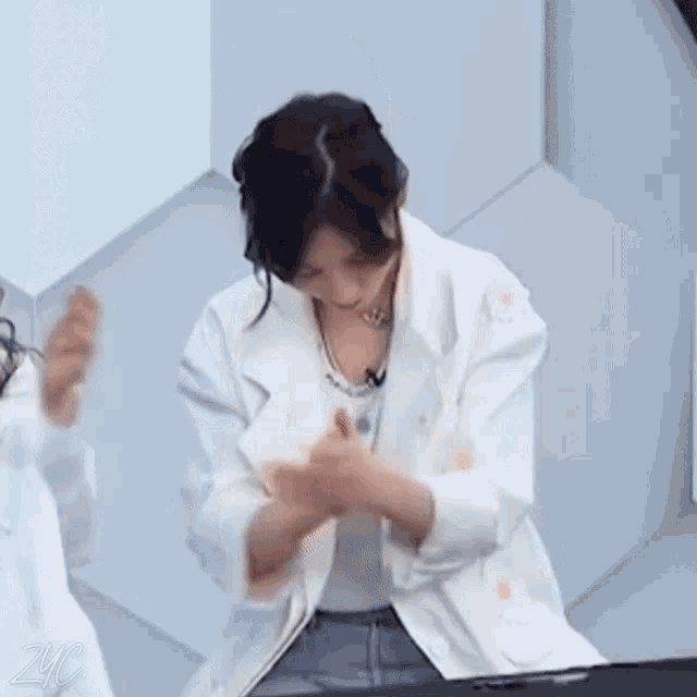 a woman in a white jacket is clapping her hands while another woman looks on .