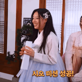 a woman in a blue dress is smiling and holding a piece of paper with korean writing on it
