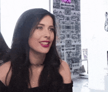 a woman with long dark hair is smiling in front of a wall with posters on it