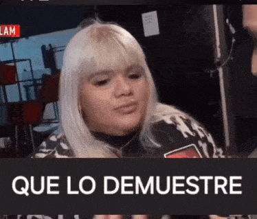 a woman with blonde hair is talking to a man and the words que lo demuestra are on the screen