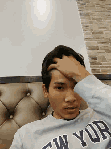 a young man wearing a new york sweatshirt is laying on a bed holding his head .