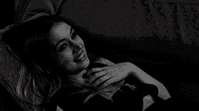 a black and white photo of a woman laying on a couch taking a selfie .