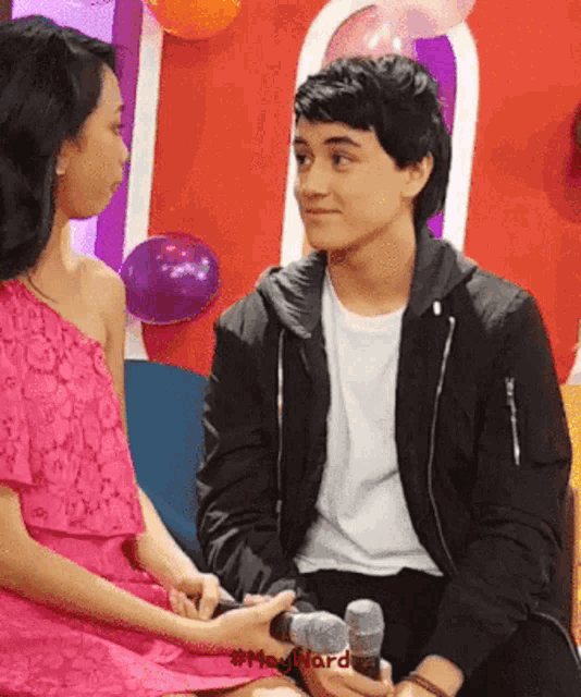 a man in a black jacket is holding a microphone next to a girl in a pink dress