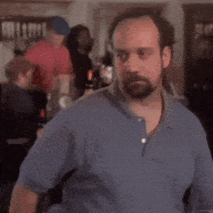 a man with a beard is sitting at a table with a crowd behind him .