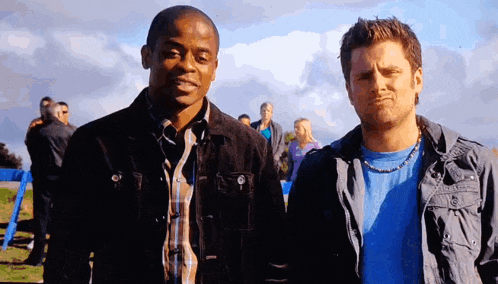two men are standing next to each other and one is wearing a blue shirt and a necklace