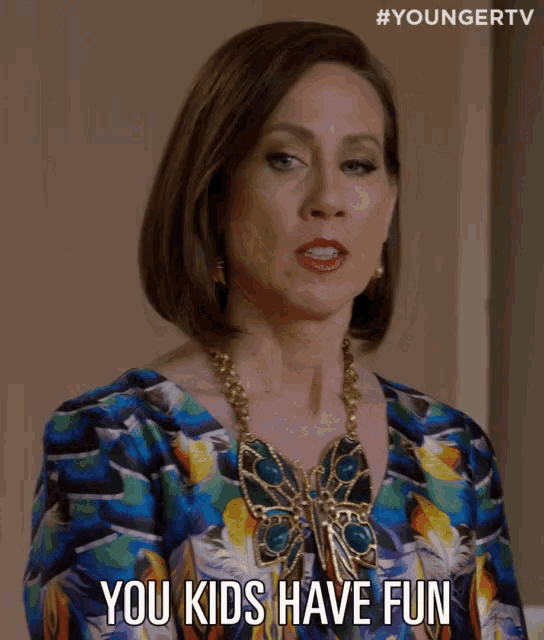 a woman wearing a colorful dress and a butterfly necklace is talking to her kids .