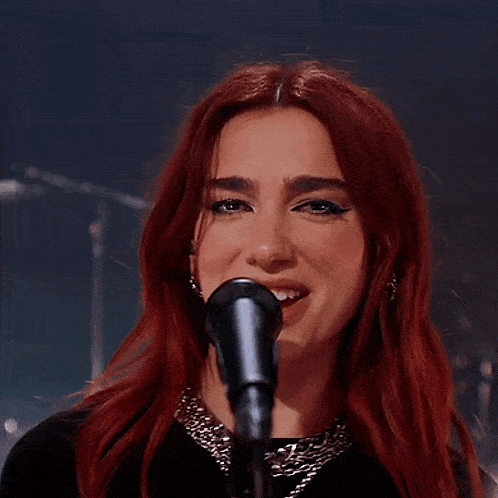a woman with red hair singing into a microphone with her hands on her head