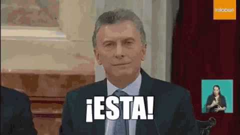 a man in a suit and tie is sitting in front of a microphone and saying `` esta '' .
