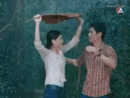 a man and a woman are standing next to each other in the rain holding an umbrella over their heads .