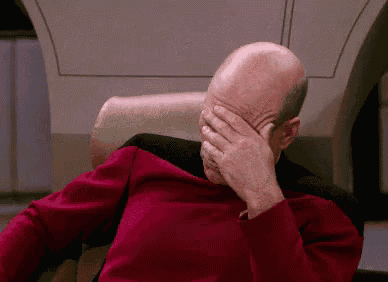 a man in a red shirt is covering his face with his hand .
