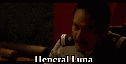 a man with a mustache is sitting in a dark room with the words `` general luna '' written on the screen .