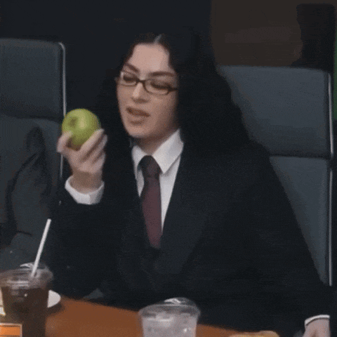 a woman in a suit and tie is holding an apple while sitting at a table .