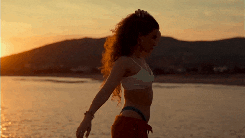 a woman in a bikini is standing in the water at sunset
