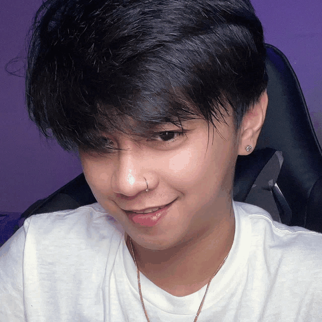 a young man wearing a nose ring and earrings smiles for the camera