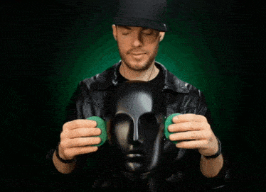 a man in a black hat is holding a green ball in front of a black mannequin head