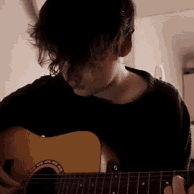 a young man is playing a guitar in a room .